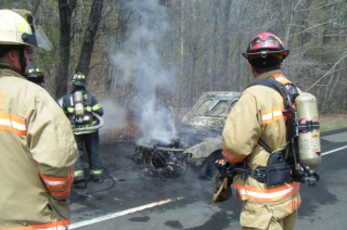 3 firefighters next to car covered in grey soot