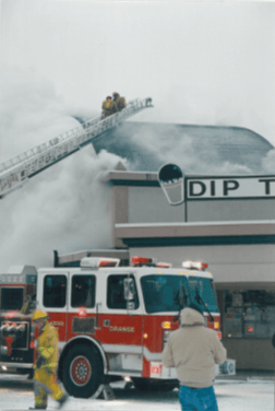 Firefighters on a fire truck ladder in front of smoking building