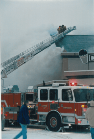 Firefighters on a fire truck ladder in front of smoking building
